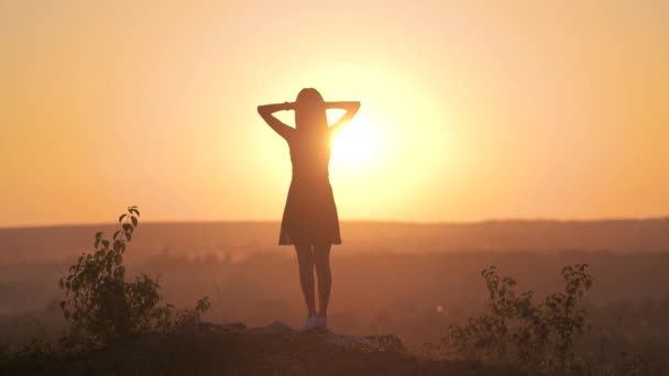 Una joven en vestido de verano levantando las manos al aire libre disfrutando de la vista de la puesta de sol de color amarillo brillante. - Metraje, vídeo