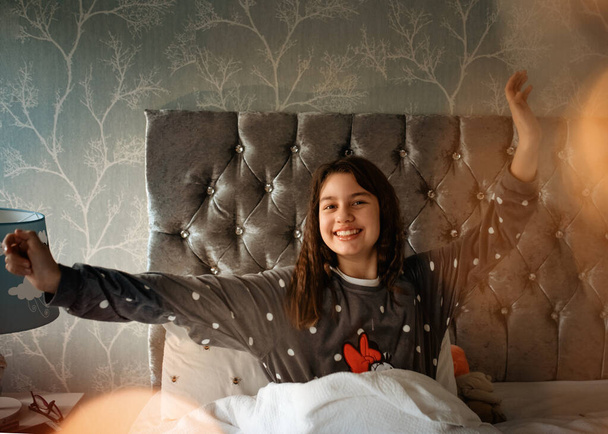 Девушки в серой пижаме, сидящие на кровати и растягивающиеся утром - Фото, изображение