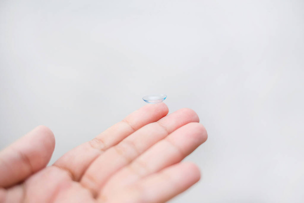 Lens on the finger. The transparent lens is on your hand. lens on a white background. Myopia. On white background with an free space - Photo, Image