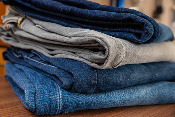 Jeans de différentes couleurs, disposés les uns sur les autres, laissant les poches visibles, et placés sur une surface en bois. - Photo, image