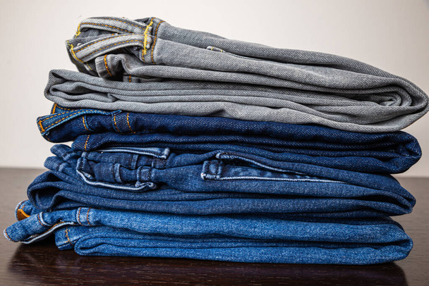 Folded jeans of various colors, arranged one on top of the other, and placed on a wooden surface. - Photo, Image
