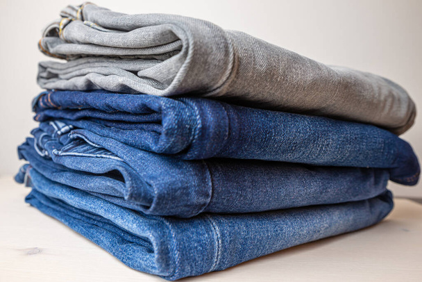 Gevouwen jeans van verschillende kleuren, boven elkaar gerangschikt en op een houten ondergrond geplaatst. - Foto, afbeelding