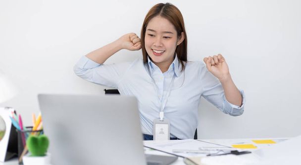 若いアジア人女性従業員はハードな朝の仕事の後にリラックスした姿勢を取っており、仕事が終わった後に仕事で休んでいる幸せな女性は、疲労が緩和され、オフィスで働く女性. - 写真・画像