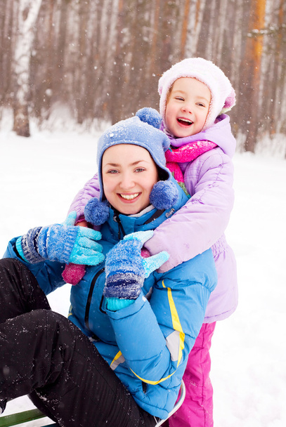 Happy family; young mother and her daughter with a sled having fun in the winter park (focus on the child) - Fotó, kép