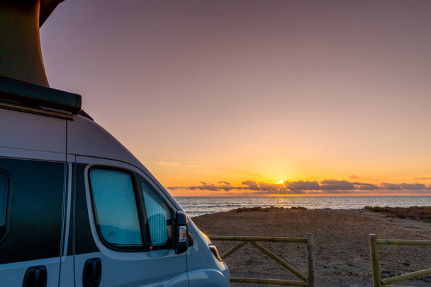 La Manga del Mar Menor, 22 февраля, 2021: красивый восход солнца с серым фургоном-кемпером с всплывающей крышей, припаркованной на пляже - Фото, изображение