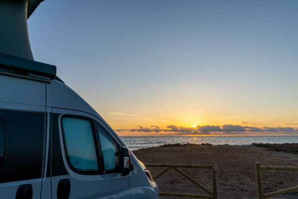 La Manga del Mar Menor, 22 febrero, 2021: hermosa salida del sol con una caravana gris con un techo emergente estacionado en la playa - Foto, imagen