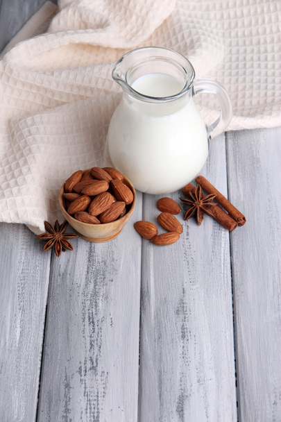 Almond milk in jug with almonds in bowl, on color wooden background - Фото, зображення