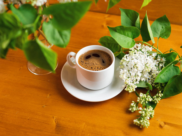 木製のテーブルの上に香り高いホットエスプレッソコーヒーの白いライラックの花束、コピースペース - 写真・画像