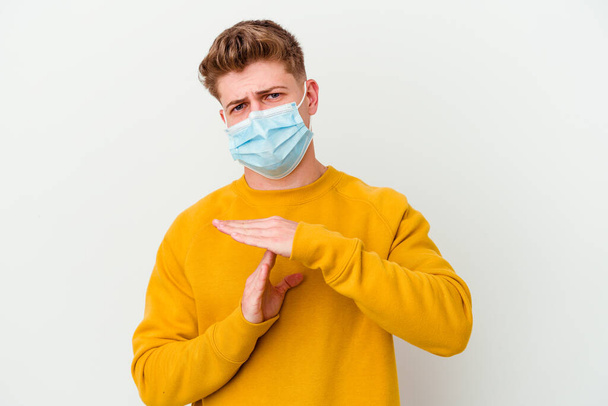 Koronavirüs maskesi takan genç bir adam beyaz arka planda izole edilmiş bir şekilde bir mola hareketi gösteriyor.. - Fotoğraf, Görsel