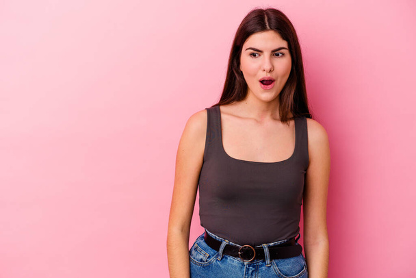 Young caucasian woman isolated on pink background being shocked because of something she has seen. - Foto, afbeelding