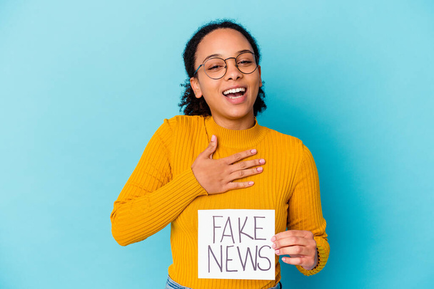 Jovem negra americana mista mulher segurando um conceito de notícias falsas ri em voz alta mantendo a mão no peito. - Foto, Imagem