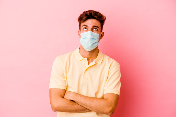 Jovem caucasiano vestindo uma proteção para coronavírus isolado em fundo rosa cansado de uma tarefa repetitiva. - Foto, Imagem