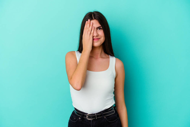 Young caucasian woman isolated on blue background having fun covering half of face with palm. - Photo, image