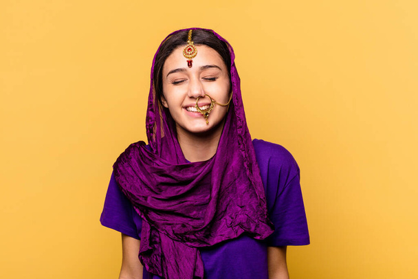 黄色の背景に隔離された伝統的なサリーを身に着けている若いインド人女性は笑い、目を閉じて、リラックスして幸せを感じています. - 写真・画像