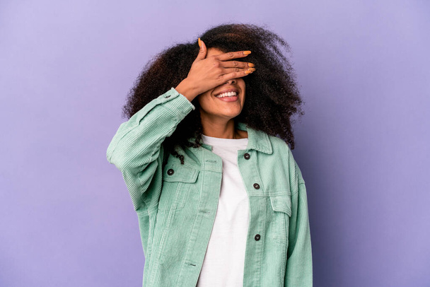 Mladý africký americký kudrnatý žena izolovaný na fialové pozadí zakrývá oči s rukama, úsměvy široce čeká na překvapení. - Fotografie, Obrázek