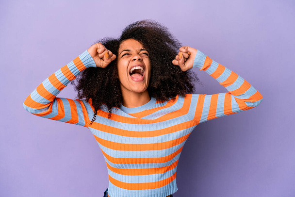 Young african american curly woman isolated on purple background raising fist after a victory, winner concept. - Foto, afbeelding
