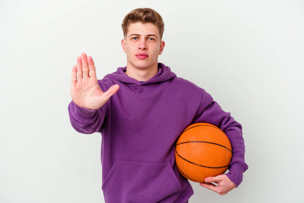 młody biały człowiek gra w koszykówkę pojedyncze tło stojąc z wyciągniętą ręką pokazując znak stopu, uniemożliwiając ci. - Zdjęcie, obraz