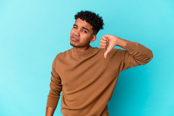 Jovem afro-americano encaracolado isolado em azul mostrando um gesto de antipatia, polegares para baixo. Conceito de desacordo. - Foto, Imagem