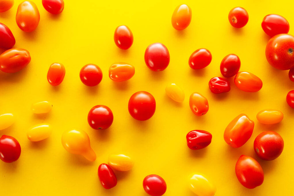 Bunch of red, orange, yellow cherry tomatoes on yellow background. Food background - Фото, зображення