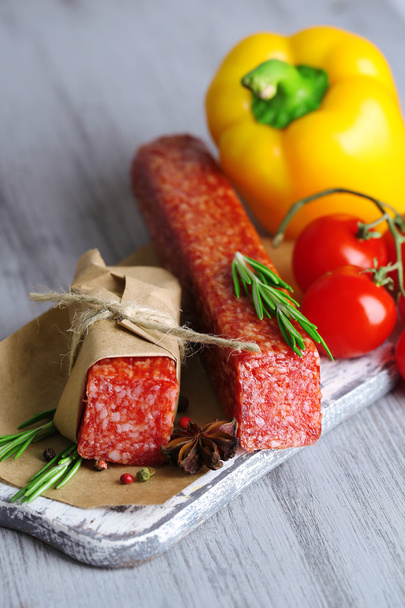 Tasty salami sausage, vegetables and spices on paper on wooden background - Foto, Bild