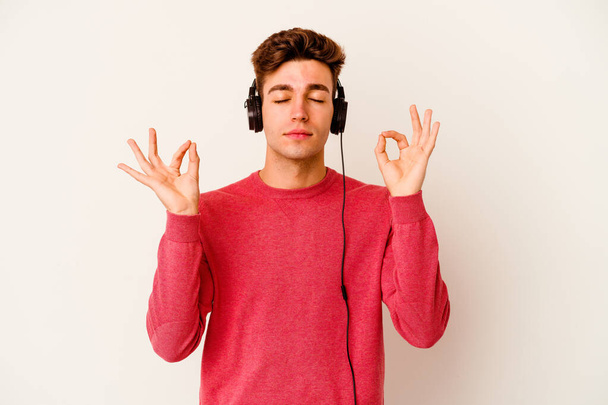 Young caucasian man listening to music isolated on white background relaxes after hard working day, she is performing yoga. - Fotografie, Obrázek