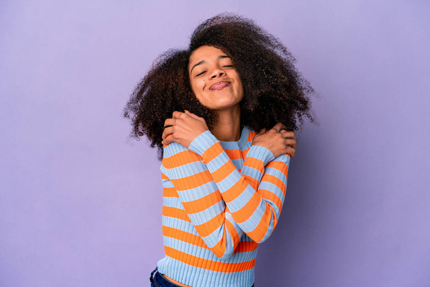 Joven mujer rizada afroamericana aislada sobre abrazos de fondo púrpura, sonriente despreocupada y feliz. - Foto, imagen
