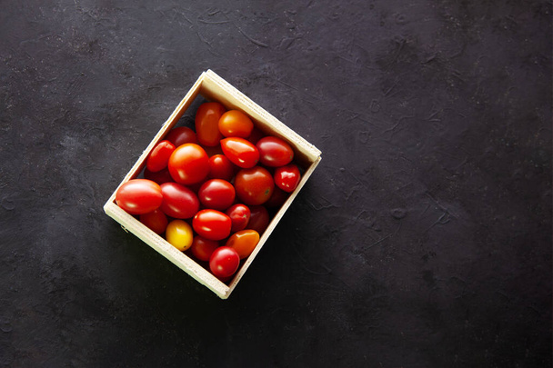 bowl and wooden box with cherry tomatoes on dark gray background. - Valokuva, kuva