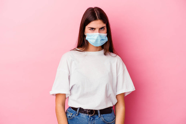 Young caucasian woman wearing a mask for virus isolated on pink background shrugs shoulders and open eyes confused. - Foto, imagen