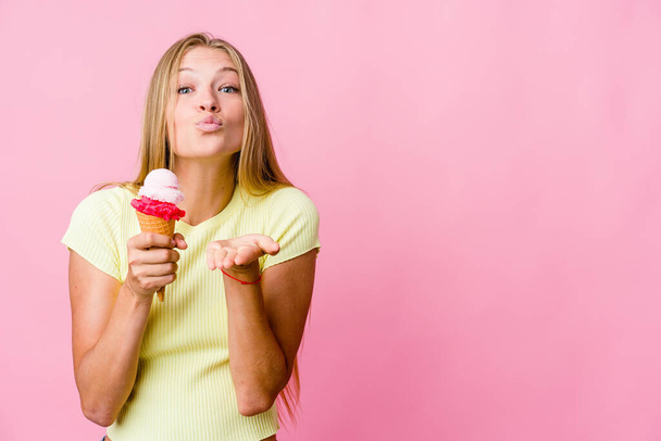 Junge russische Frau isst ein Eis isoliert faltbare Lippen und hält Handflächen, um Luftkuss zu senden. - Foto, Bild