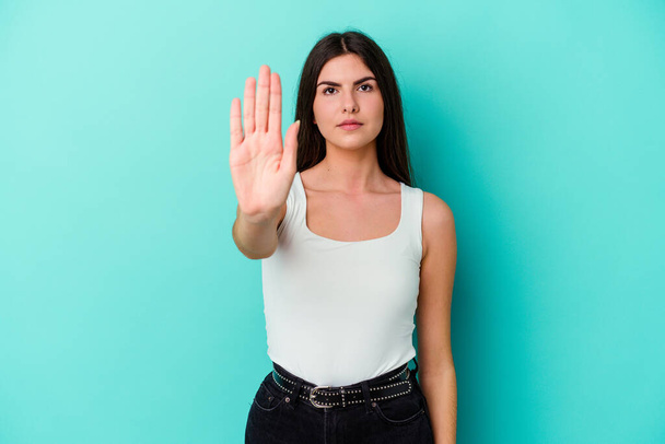 Young caucasian woman isolated on blue background standing with outstretched hand showing stop sign, preventing you. - Foto, Bild