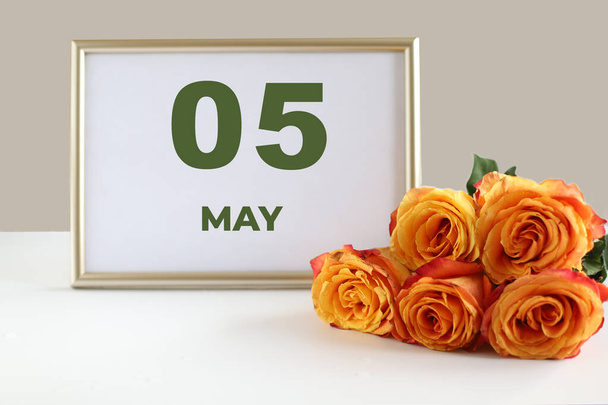 dzień miesiąca 05 Maj kalendarz ramka fotograficzna i żółta róża na białym stole. - Zdjęcie, obraz