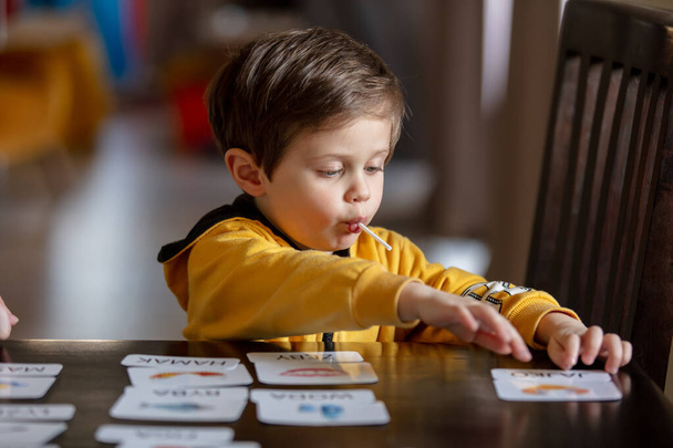 маленький мальчик учит слова из карт в рамках программы ABA терапии дома за столом  - Фото, изображение