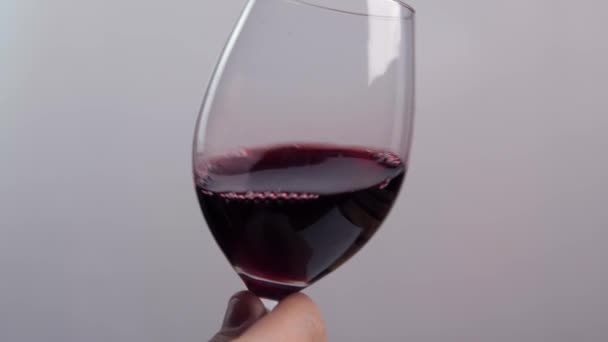 Ręka mężczyzny lekko potrząsa szklanym kieliszkiem, w którym znajduje się czerwone wino. Koncepcja alkoholu - Materiał filmowy, wideo