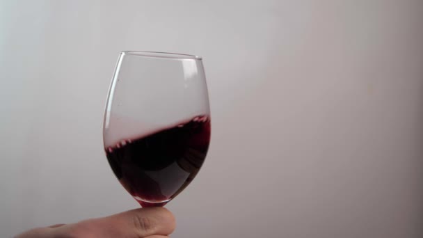 Die Hand eines Mannes schüttelt leicht einen Glaskelch, in dem Rotwein ist. Alkoholkonzept - Filmmaterial, Video
