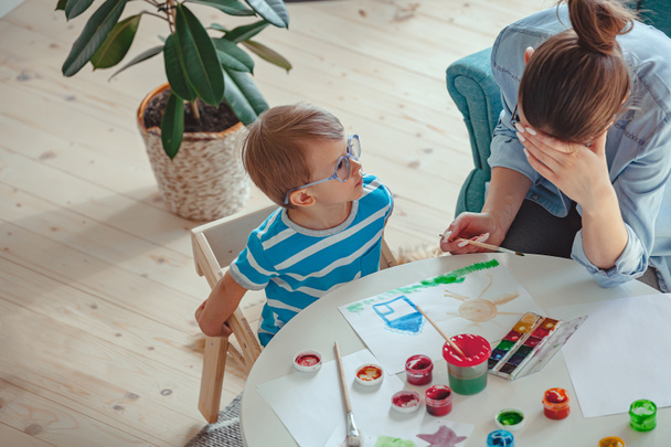 Втомлена мати і дитина з аутизмом фарбують акварель вдома
 - Фото, зображення