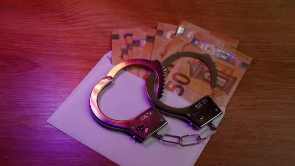 Polizeihandschellen liegen auf dem Eurogeld in einem Umschlag, der auf einem Holztisch liegt. Die Lichter der Polizei blinken. Verstoß gegen Gesetz und Gefängniskonzept - Filmmaterial, Video