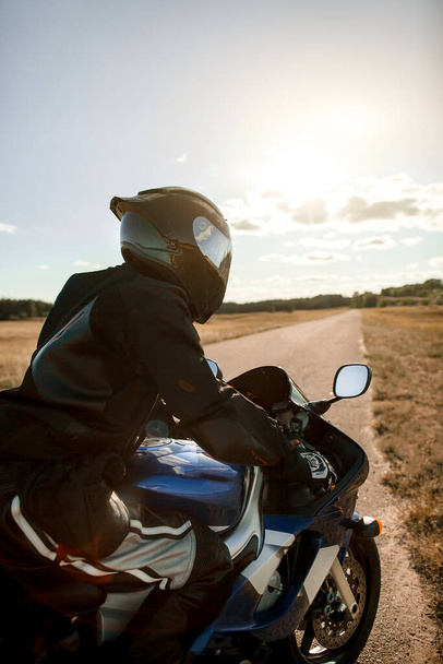 Biker or motorcyclist in a black leather suit and helmet sits on a sports motorcycle and looks into the distance. Vertical photo orientation - Photo, Image