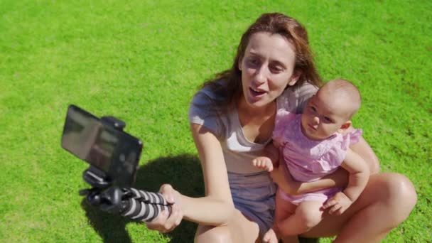 Madre blogger con figlioletta divertirsi registra un video blog su erba verde. - Filmati, video