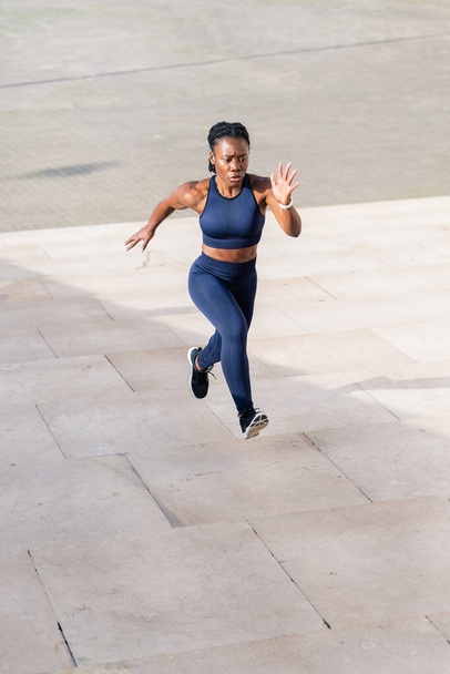 black afro girl dressed as a runner running up a flight of steps in the city at sunset - Φωτογραφία, εικόνα