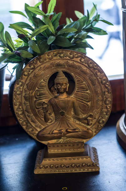 Статуэтка Будды на фоне бронзовых кругов. Сакральная фигурка в интерьере. - Фото, изображение