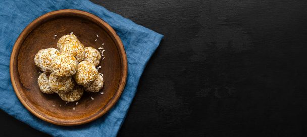 banner home made nutritious energy balls consisting of nuts, oatmeal, honey, dried fruits on a clay plate on a dark black slate background with a blue towel with place for text. healthy snack - Fotografie, Obrázek