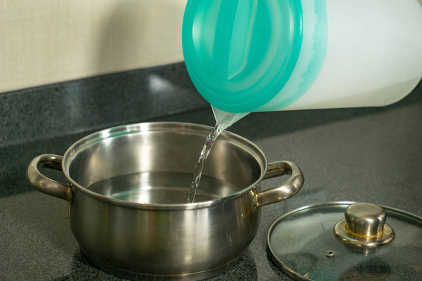 giet water uit kruik in kookpot - Foto, afbeelding