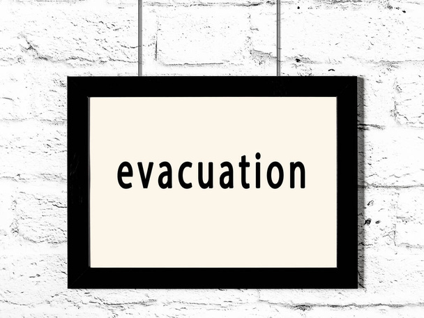Černý dřevěný rám s nápisem evakuace visí na bílé cihlové zdi  - Fotografie, Obrázek