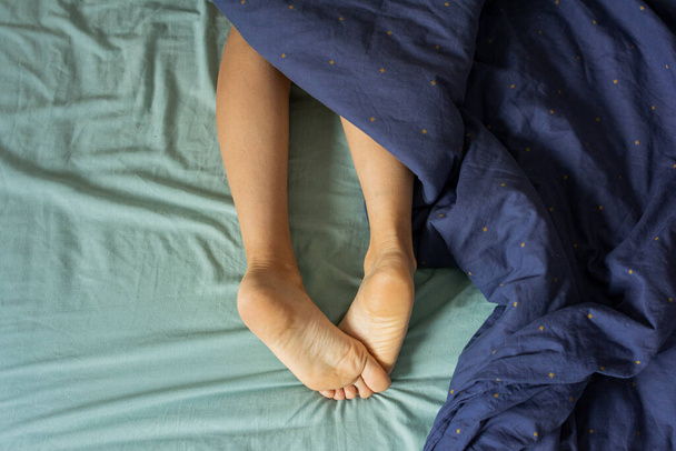Детальный снимок с копировальным пространством ног белой женщины, скрещенный снаружи одеяла, которое покрывает остальную часть её тела.. - Фото, изображение