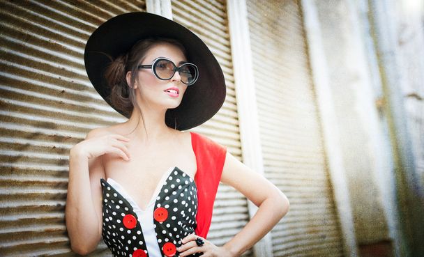 Attractive brunette girl with black hat, red scarf and sunglasses posing outdoor. Beautiful fashionable young woman with modern accessories, urban shot. Gorgeous brunette with large black hat smiling. - Foto, afbeelding