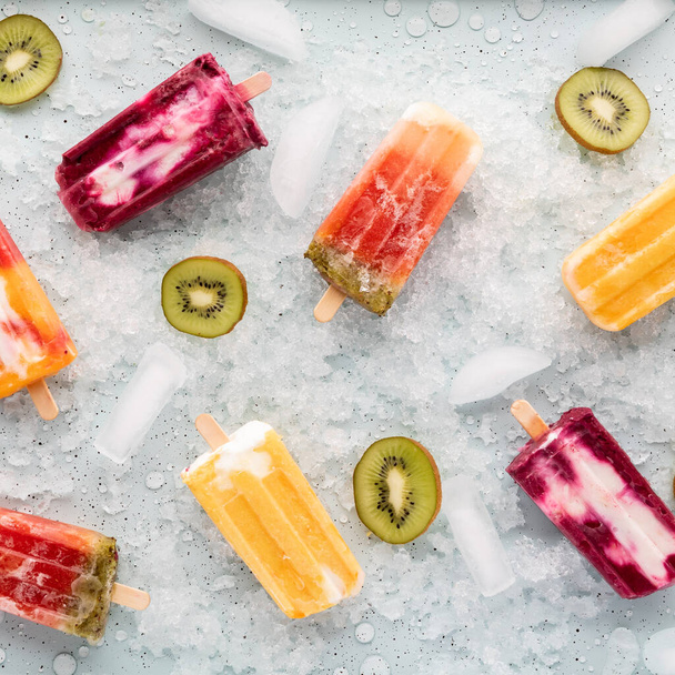 Top down view of various homemade popsicles on a tray of ice with slices of kiwi. - Photo, Image