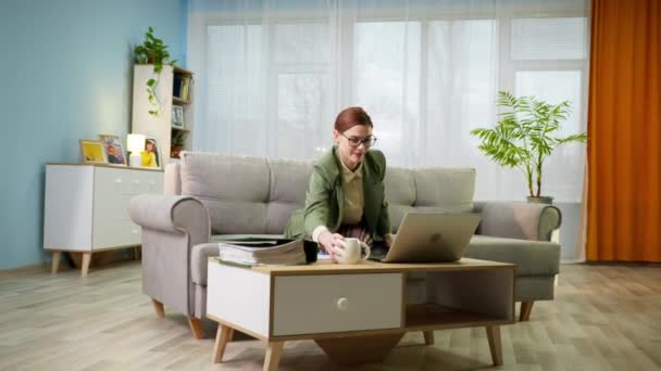 nő zakóban és pizsamában dolgozik távolról otthon, és fut egy csésze vízzel a kezében a laptop videohívás alatt ül a kanapén a szobában, zárlat - Felvétel, videó