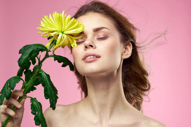 Menina bonita com uma flor amarela em um fundo rosa nua ombros maquiagem - Foto, Imagem