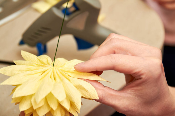 Mujer hacer diseño floral. Chica pega los pétalos de una flor artificial con una pistola de pegamento. Primer plano, enfoque selectivo - Foto, Imagen
