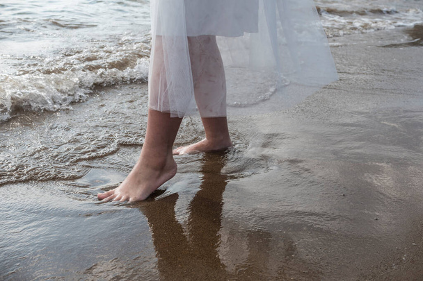 Una giovane donna immerge i piedi nudi nella dolce onda della marea in arrivo. Romantico viaggio vagabondo o tema di nozze in spiaggia. - Foto, immagini